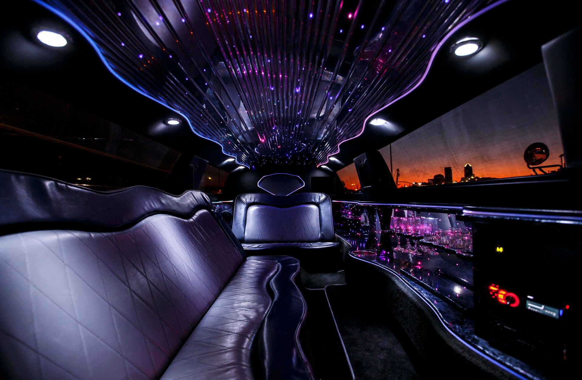 Luxury car interior with purple LED ceiling lights and city sunset visible through the windows