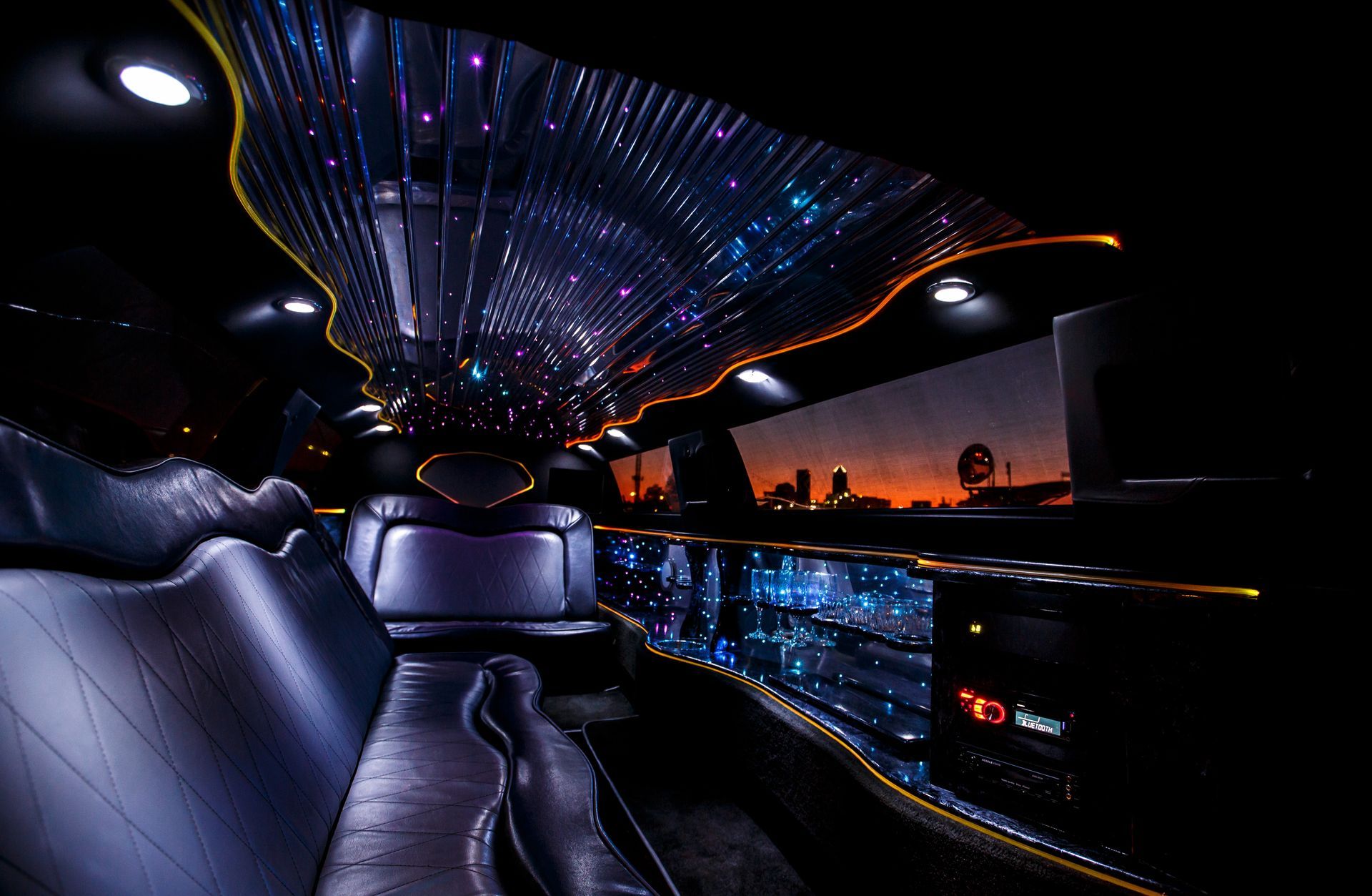 Luxury limousine interior with starry ceiling lights and blue leather seats at sunset.
