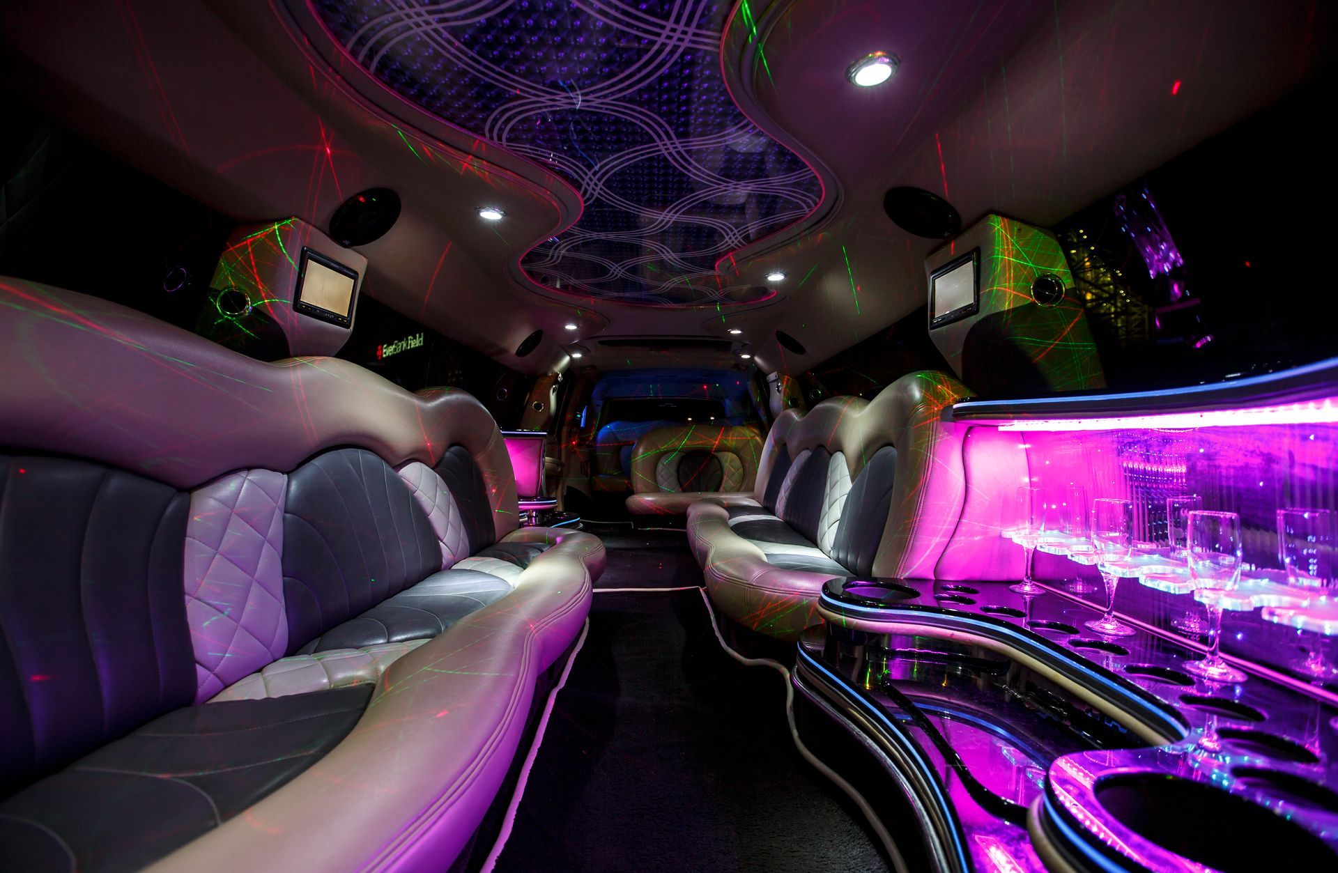 Inside a neon-lit limousine interior with black leather seats and purple ambient lighting