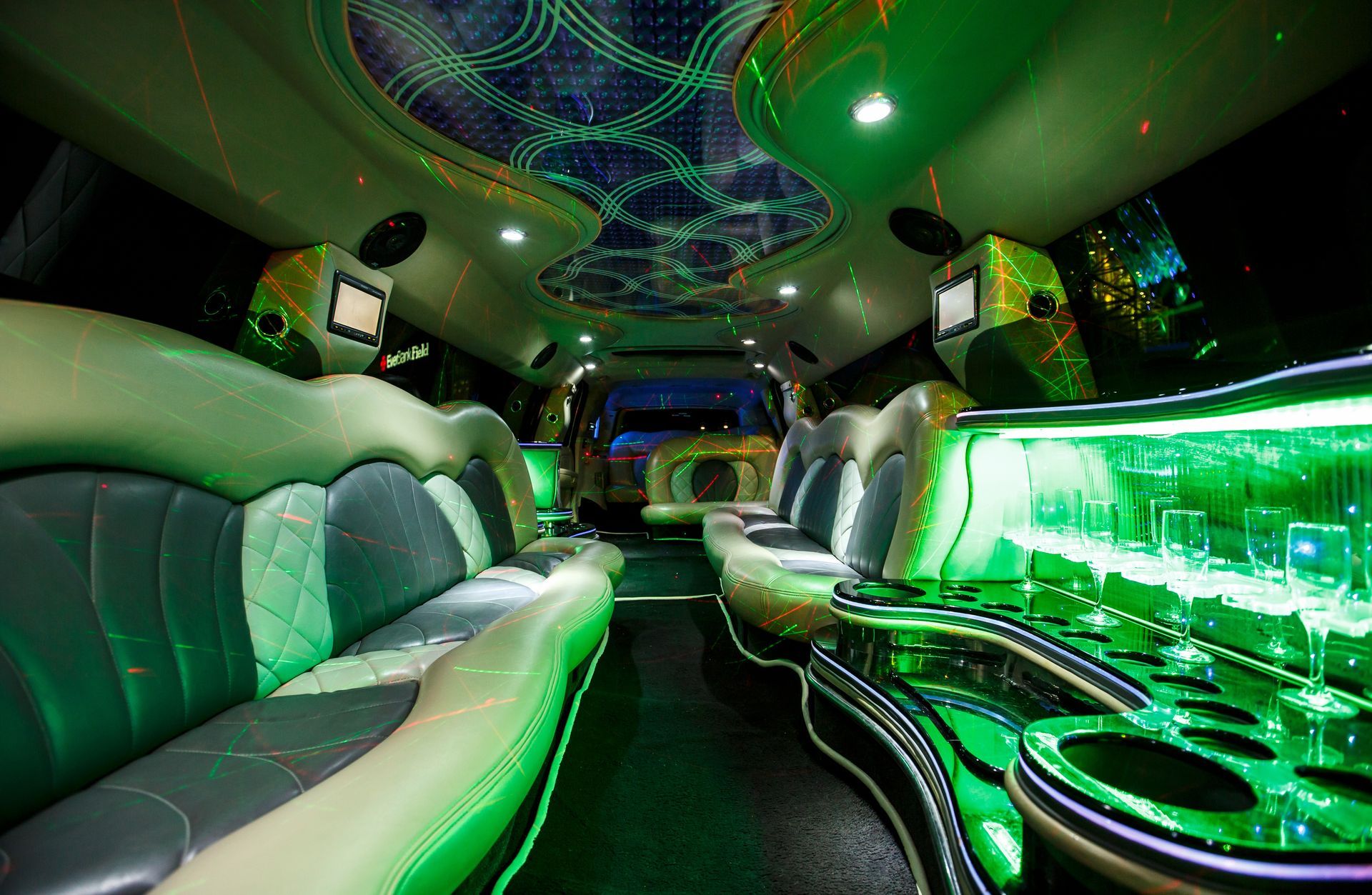 Luxury limousine interior with green neon lighting, leather seats, and glowing bar area