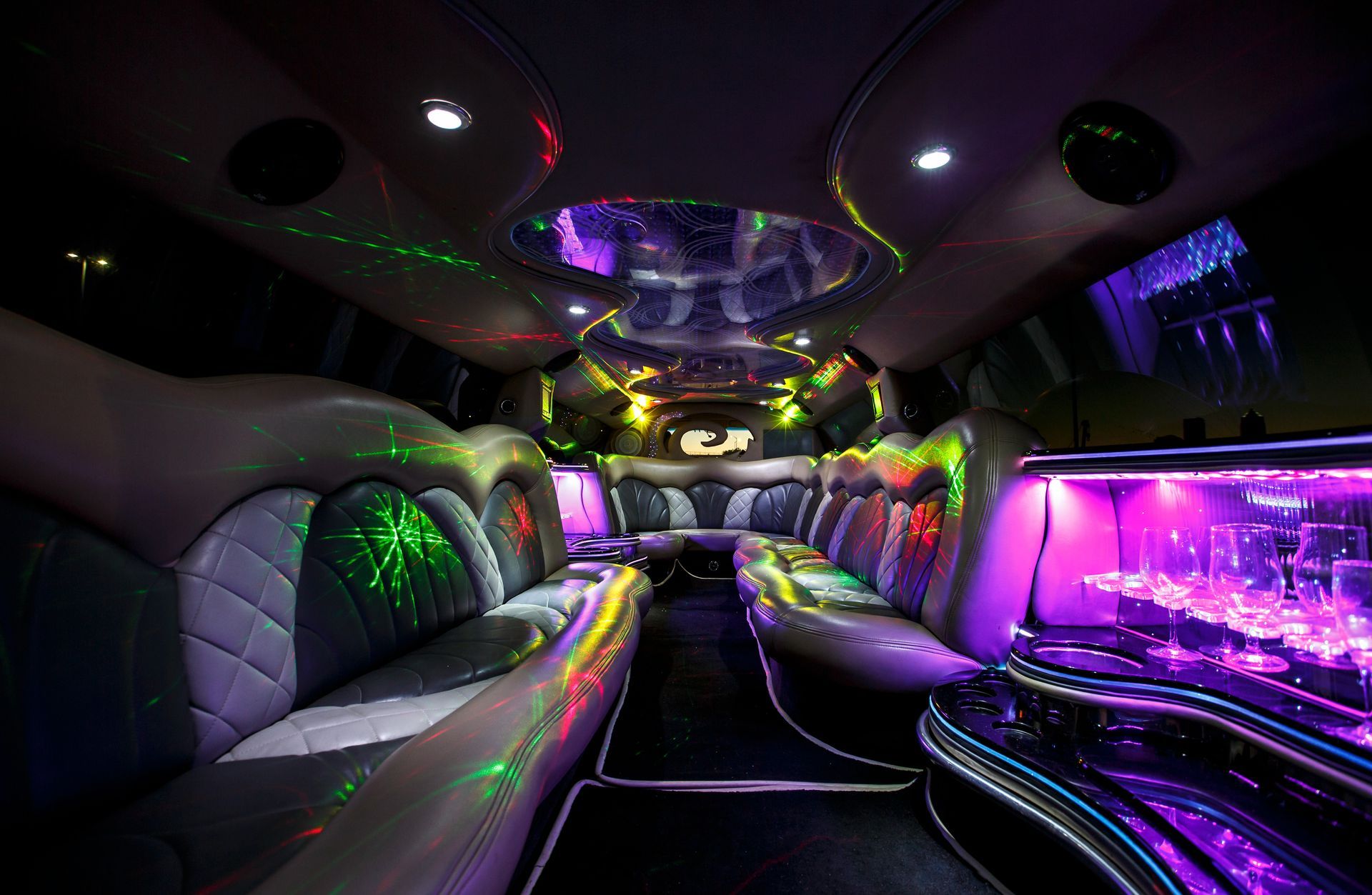 Neon-lit limousine interior with purple and green lighting, leather seats, and glossy black trim
