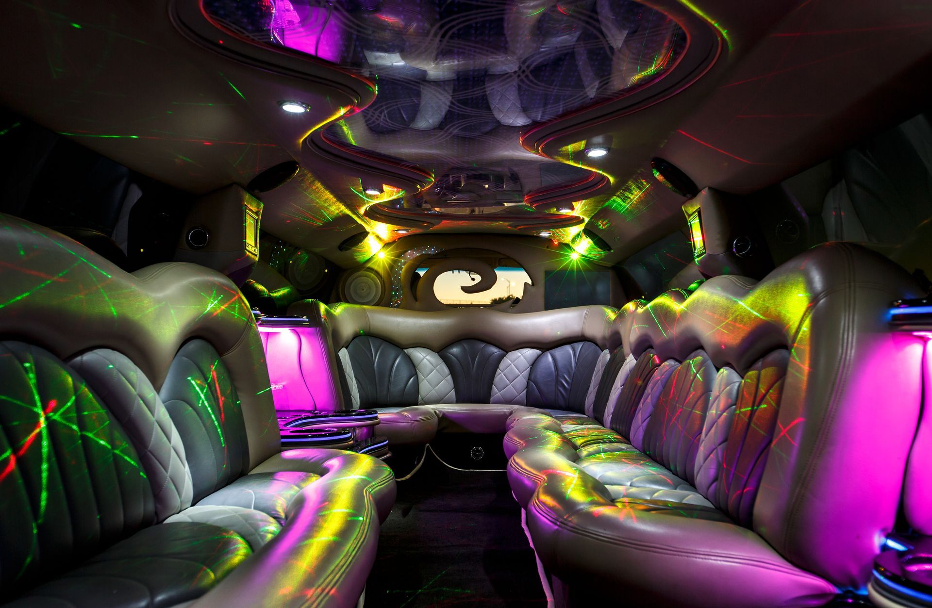 Luxurious limo interior with black leather seats, neon pink, green, and yellow lighting, and a mirrored ceiling