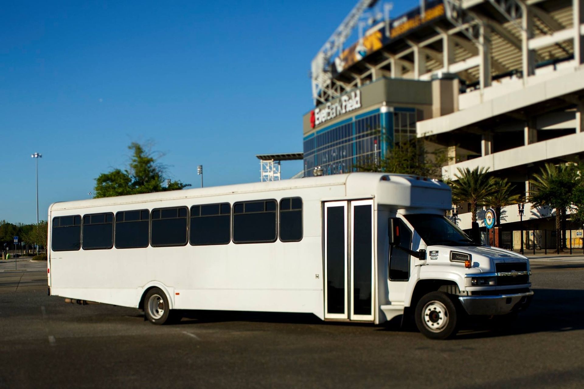 White shuttle bus parked outside a stadium on a sunny day