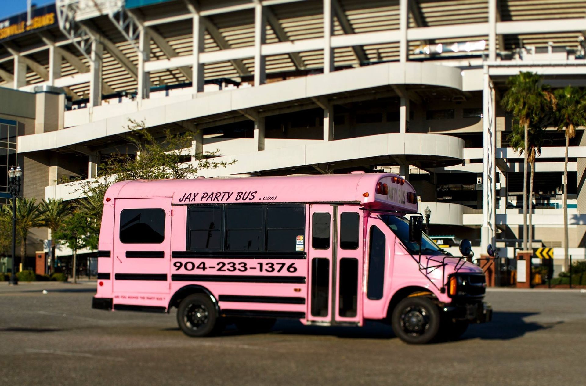 Pink shuttle bus parked outside a stadium with black text and phone number on the side