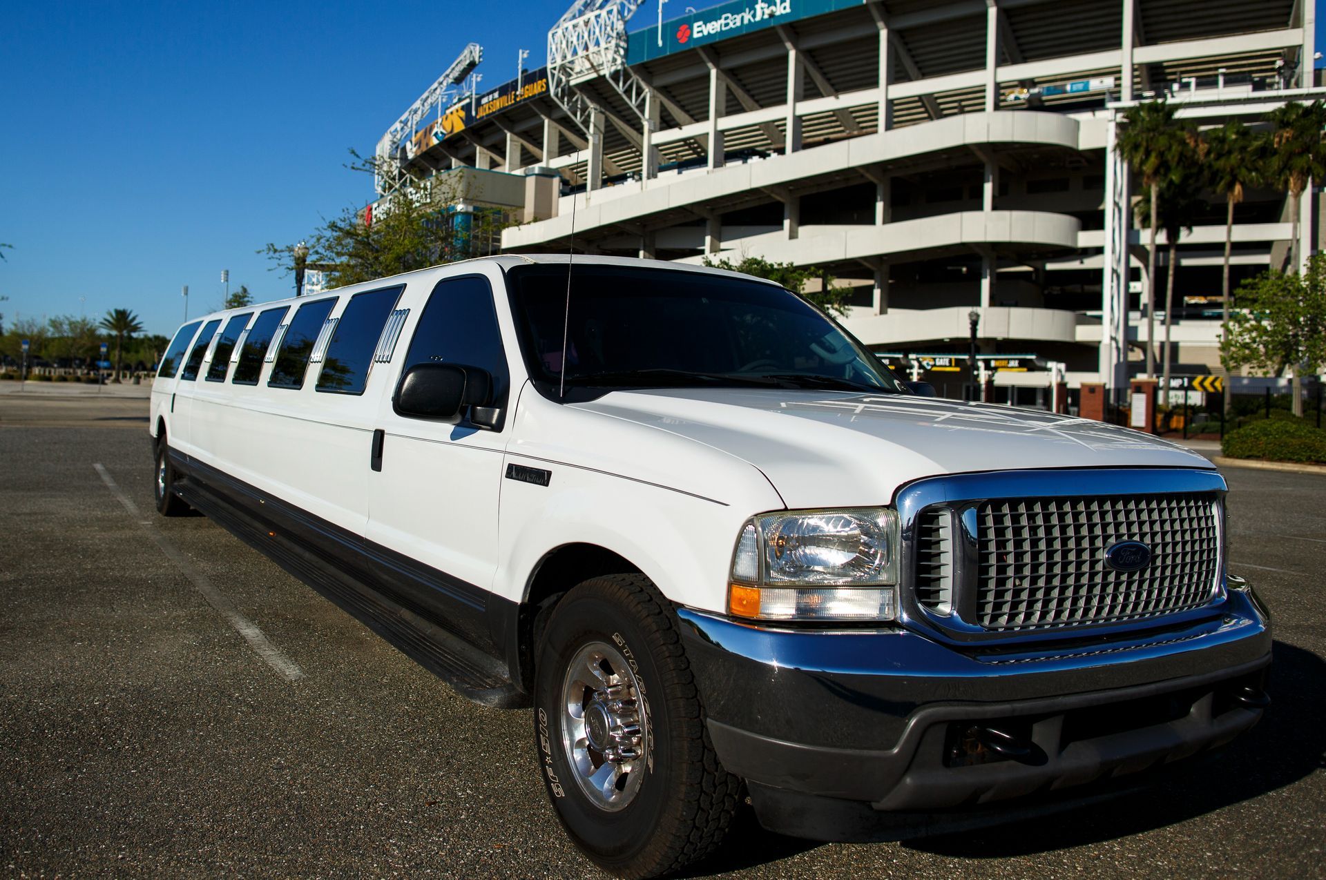 White stretch limousine parked outside a stadium on a sunny day