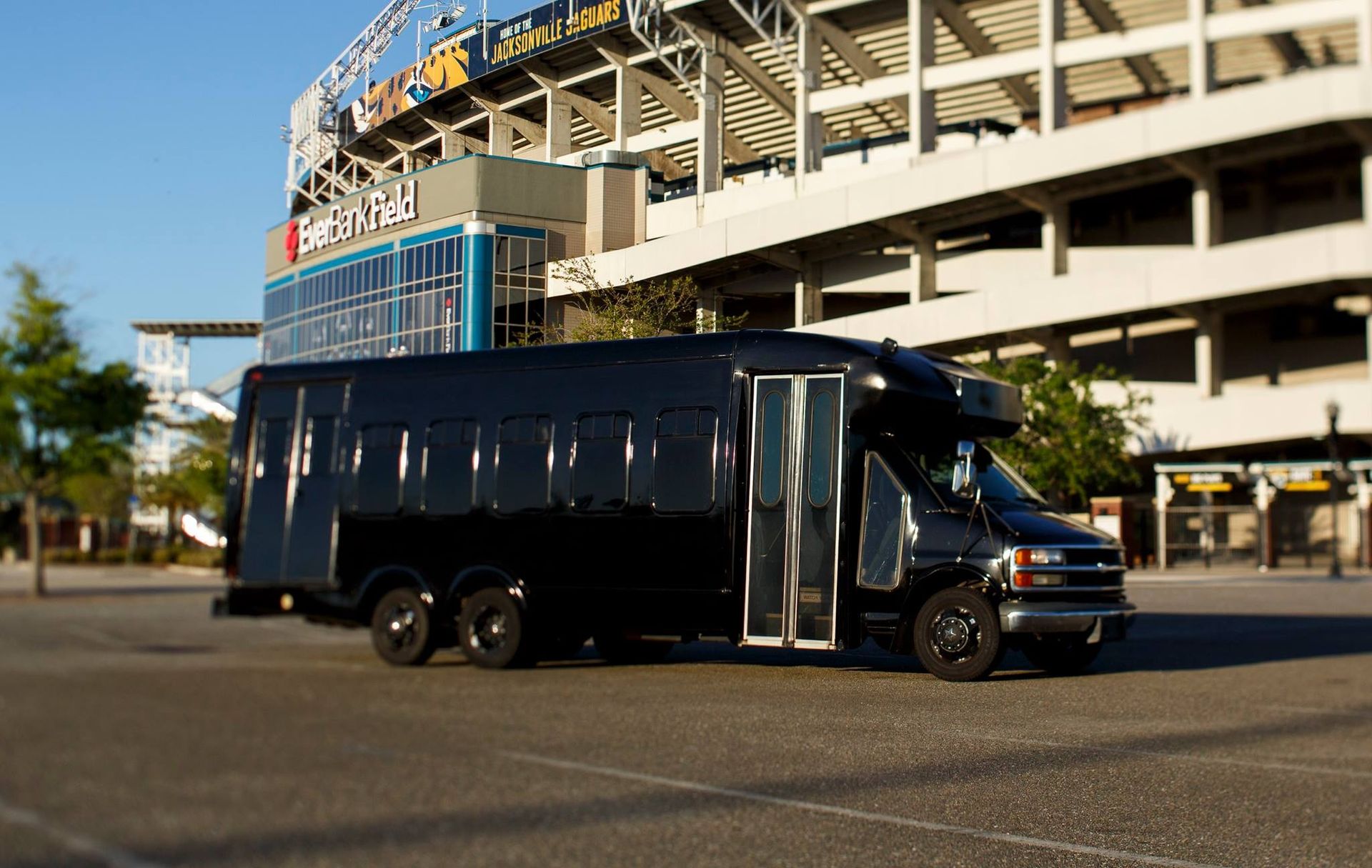 Black luxury bus parked near a stadium on a sunny day