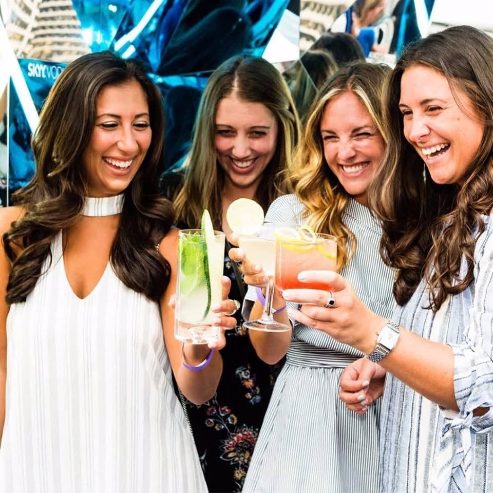 Four friends smiling and toasting colorful drinks at a lively party