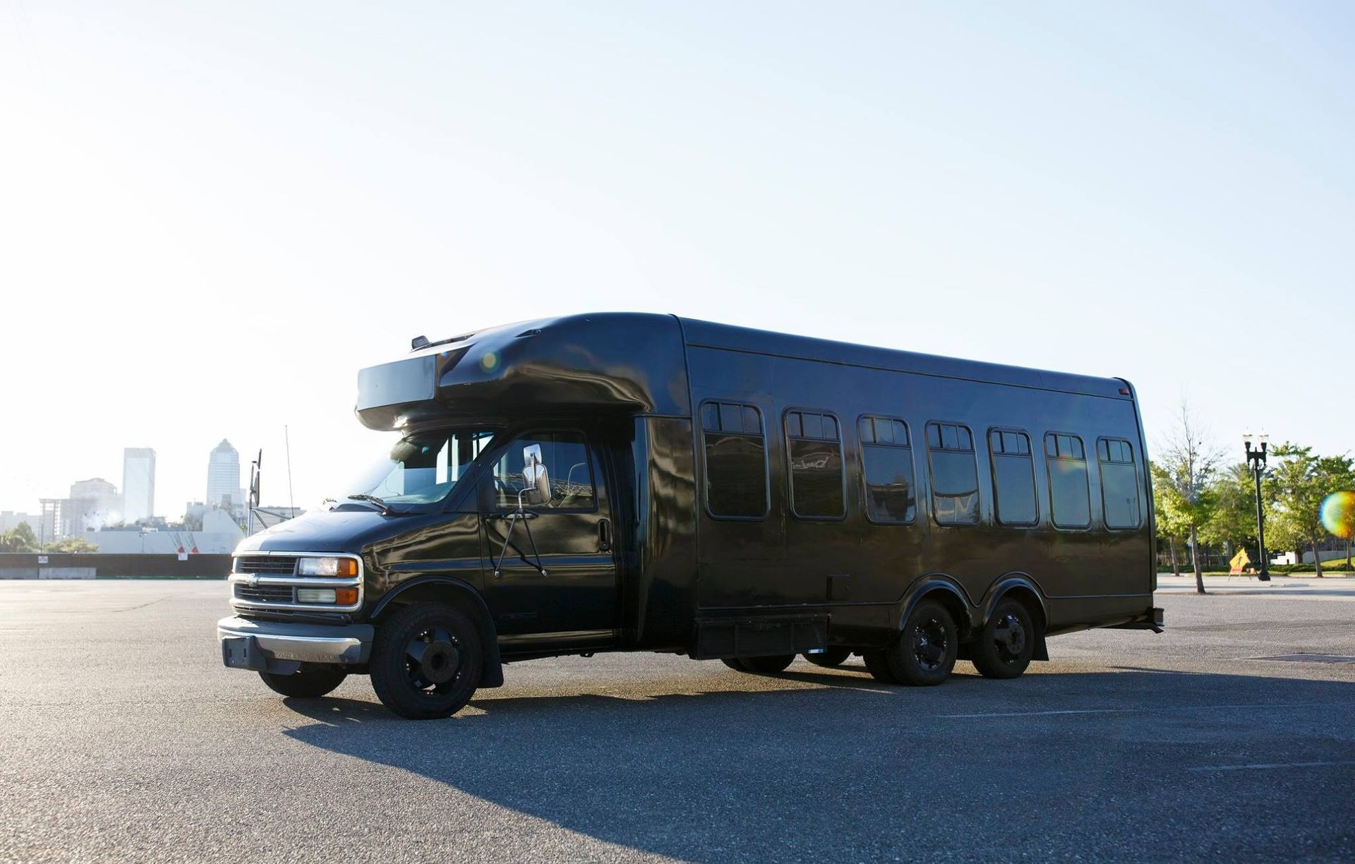 Black bus parked on an empty road near a waterfront skyline in bright sunlight