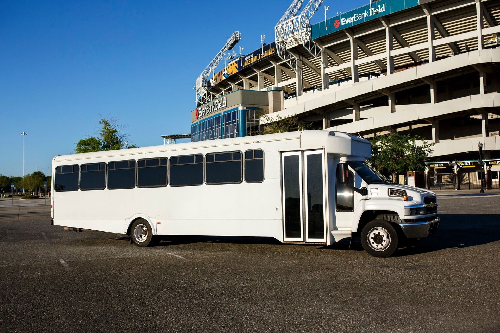 White shuttle bus parked beside a stadium on a sunny day