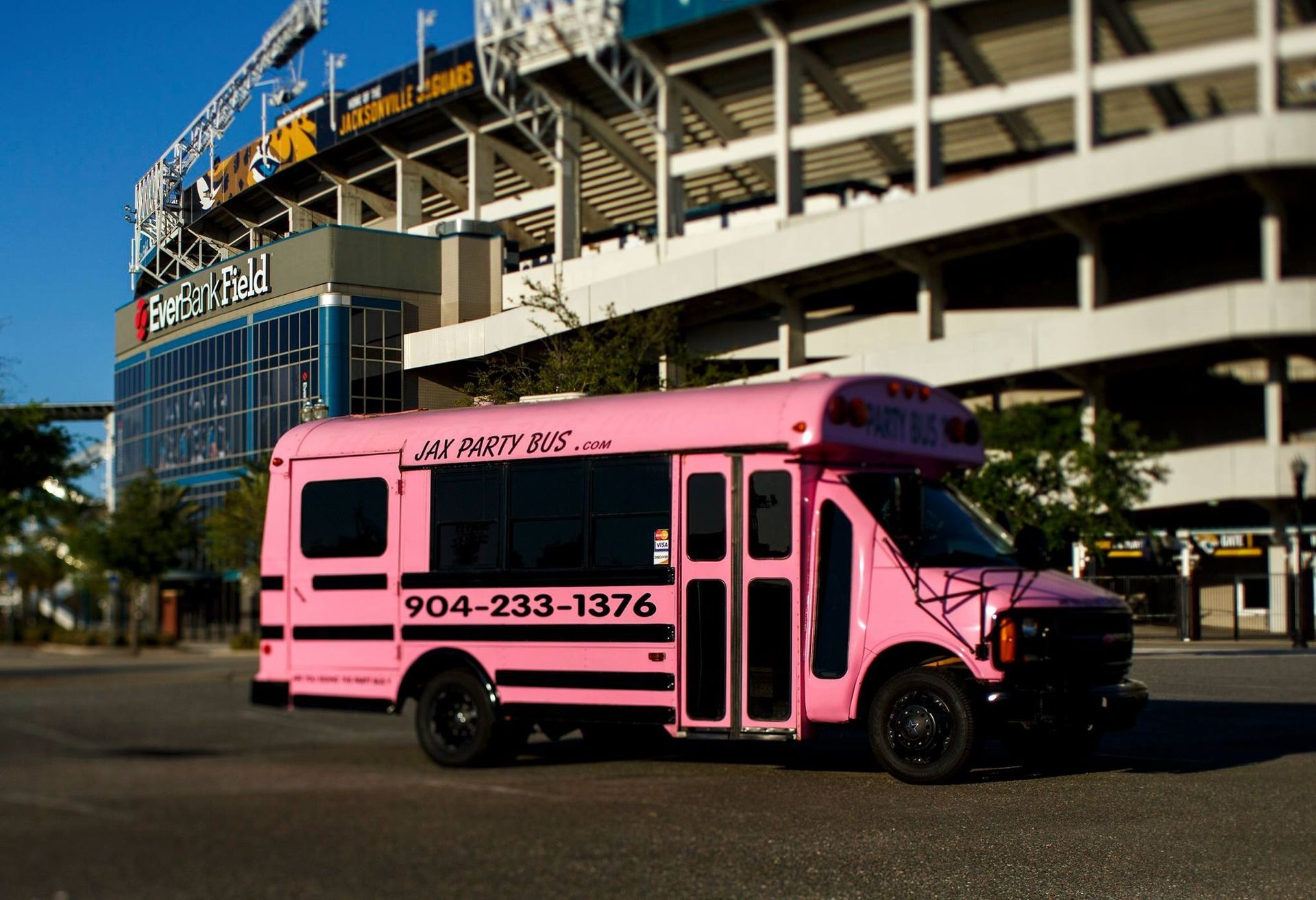 Pink city bus parked outside a stadium with a large parking structure in the background