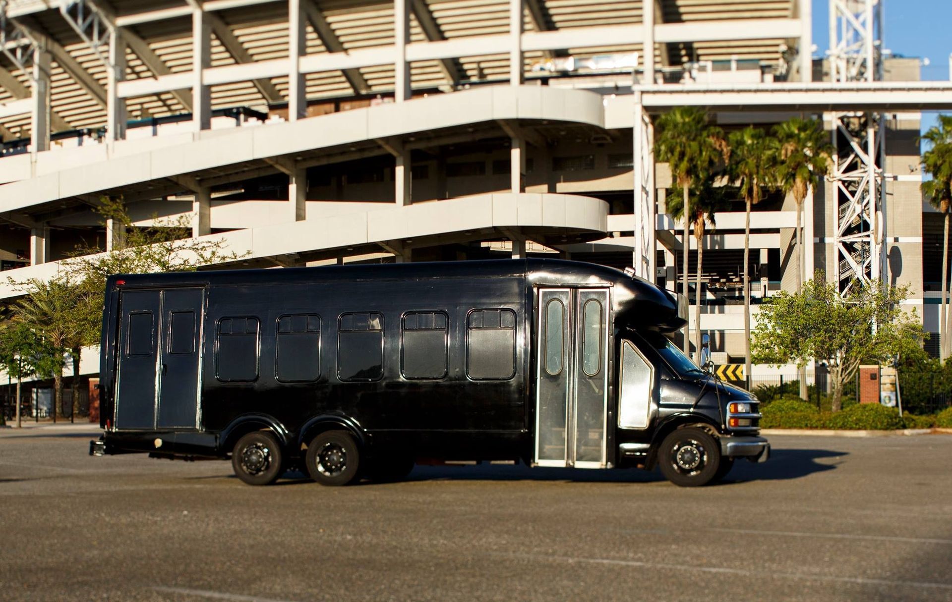 Black armored bus parked beside a stadium under bright daylight