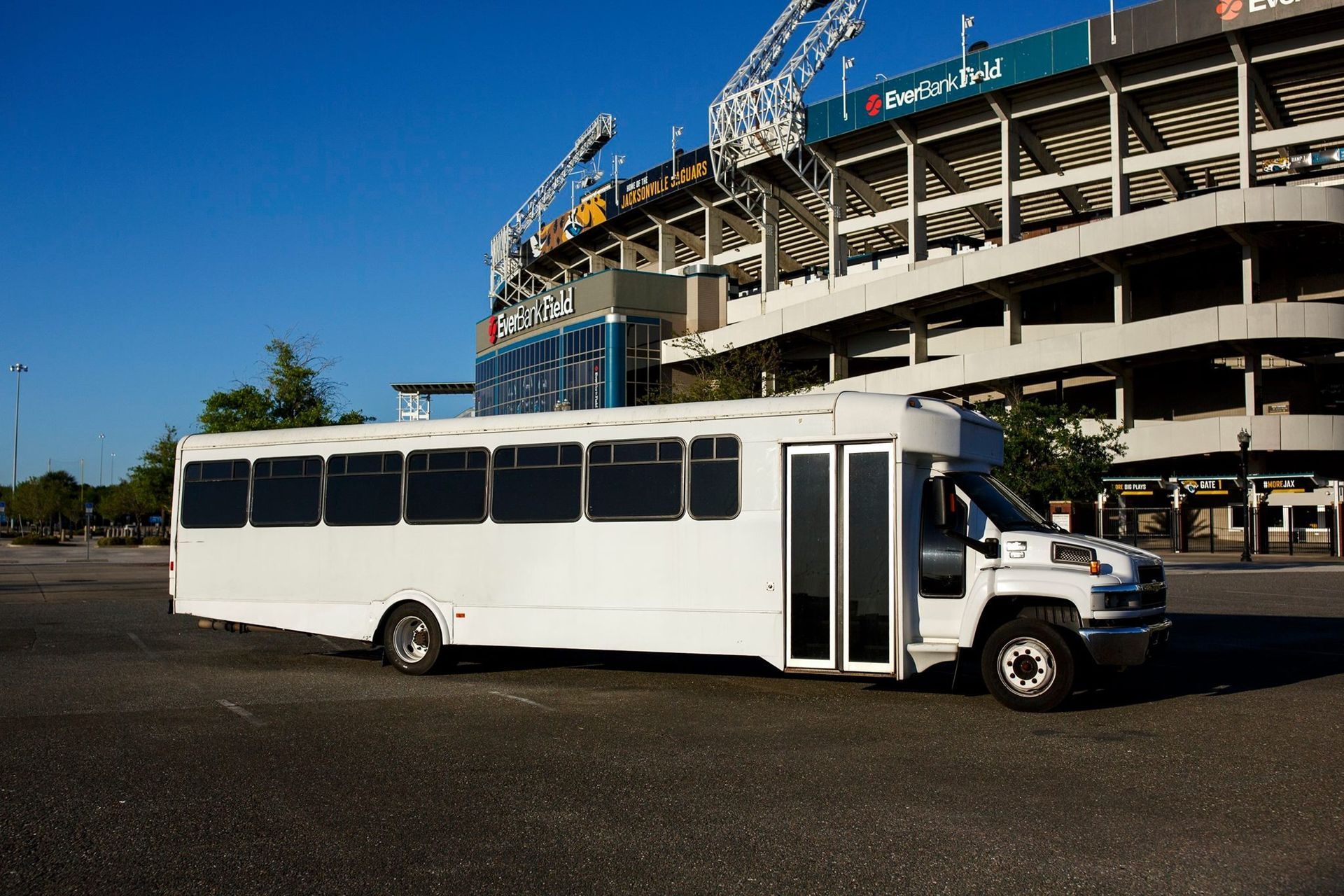 White shuttle bus parked beside a stadium under construction on a sunny day