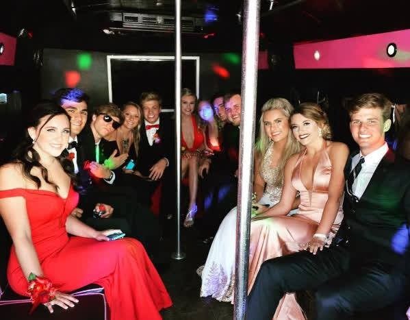 Passengers in formalwear seated inside a party bus with neon lights and a dance pole
