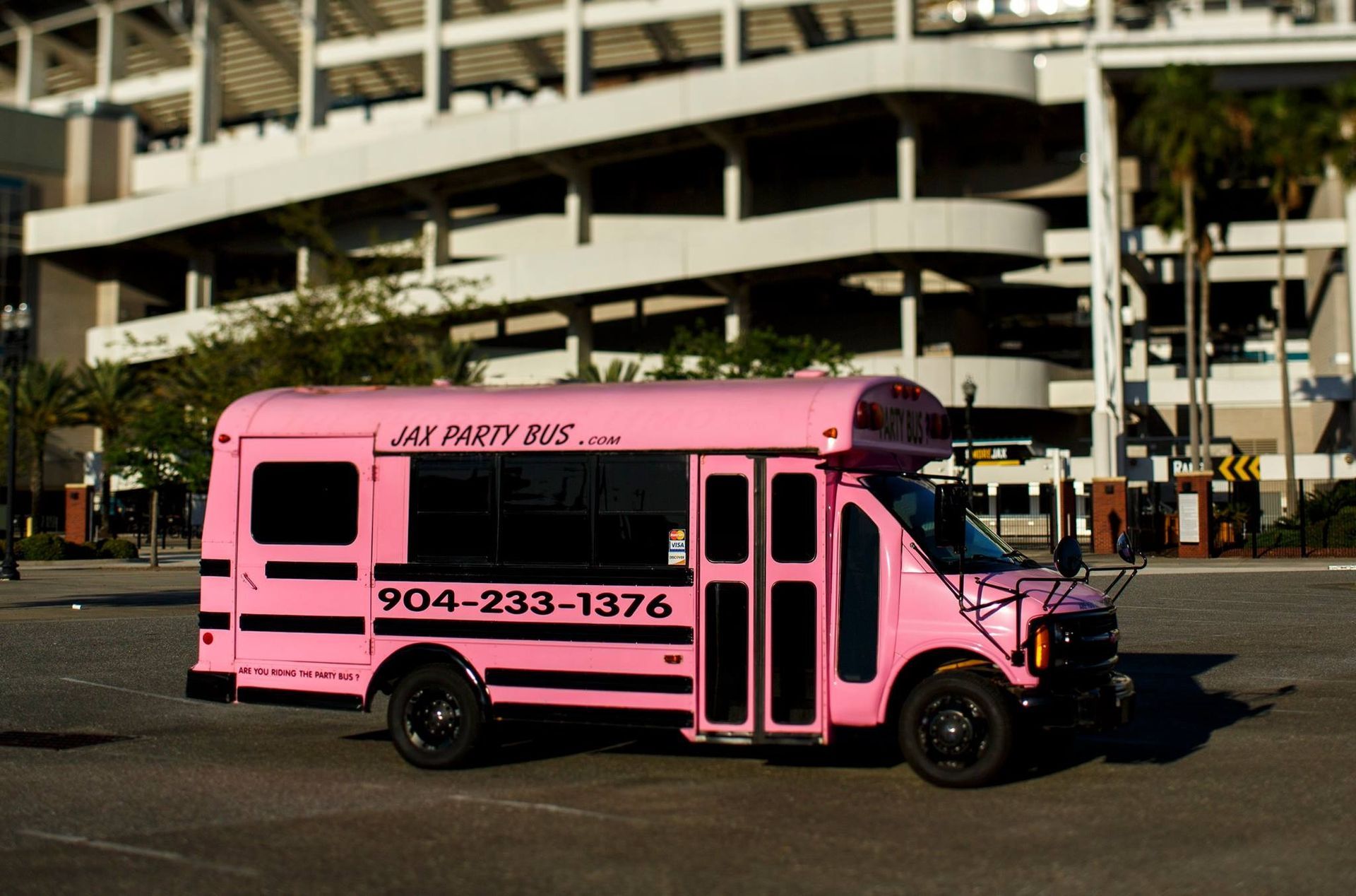 Pink shuttle bus parked in front of a building, with black lettering and stripes.