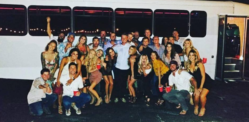 Large group posing in front of a bus at night, smiling and raising their arms