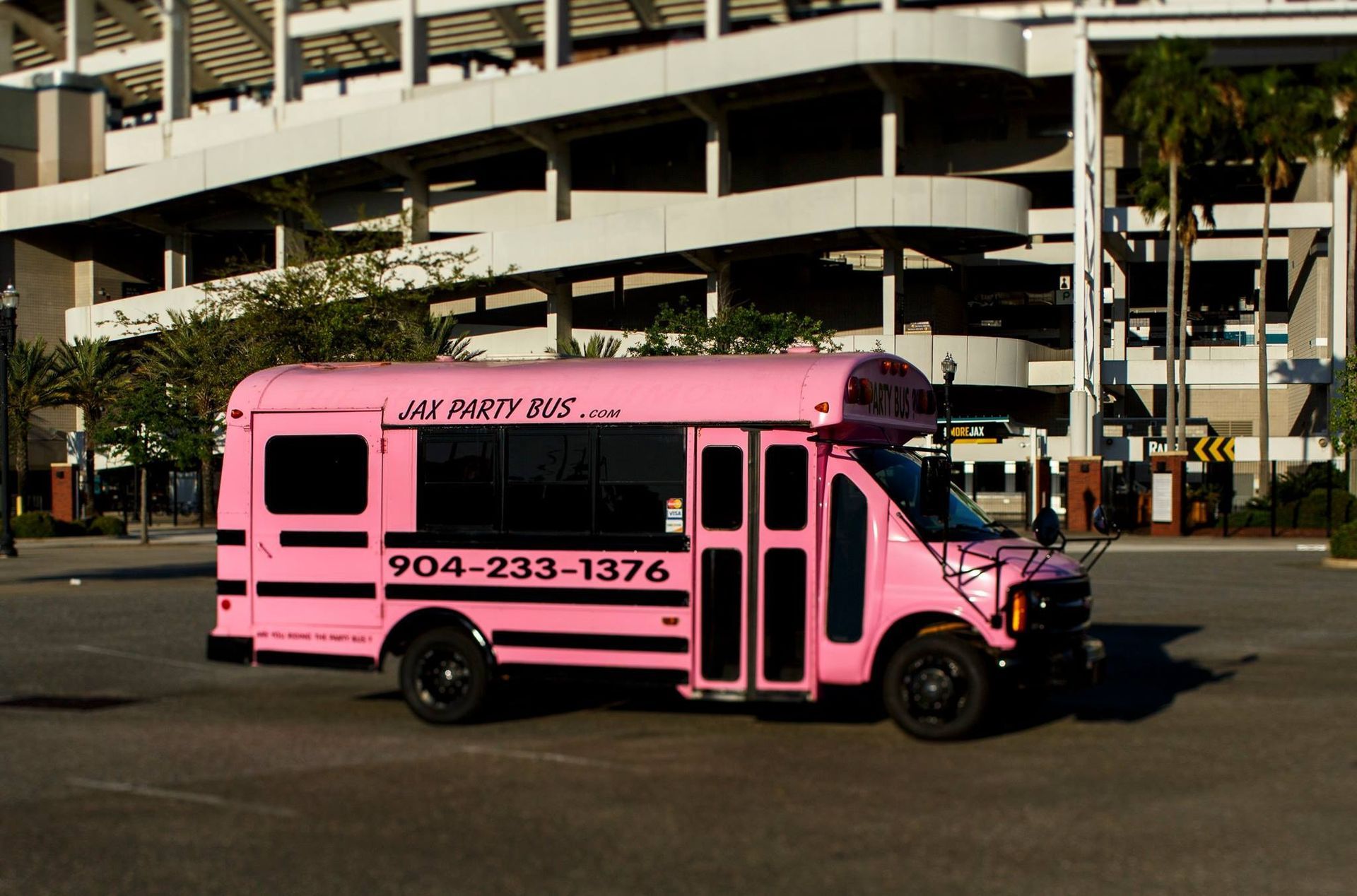 Pink shuttle bus parked outside a multi-level garage, marked with phone number 904-233-1376