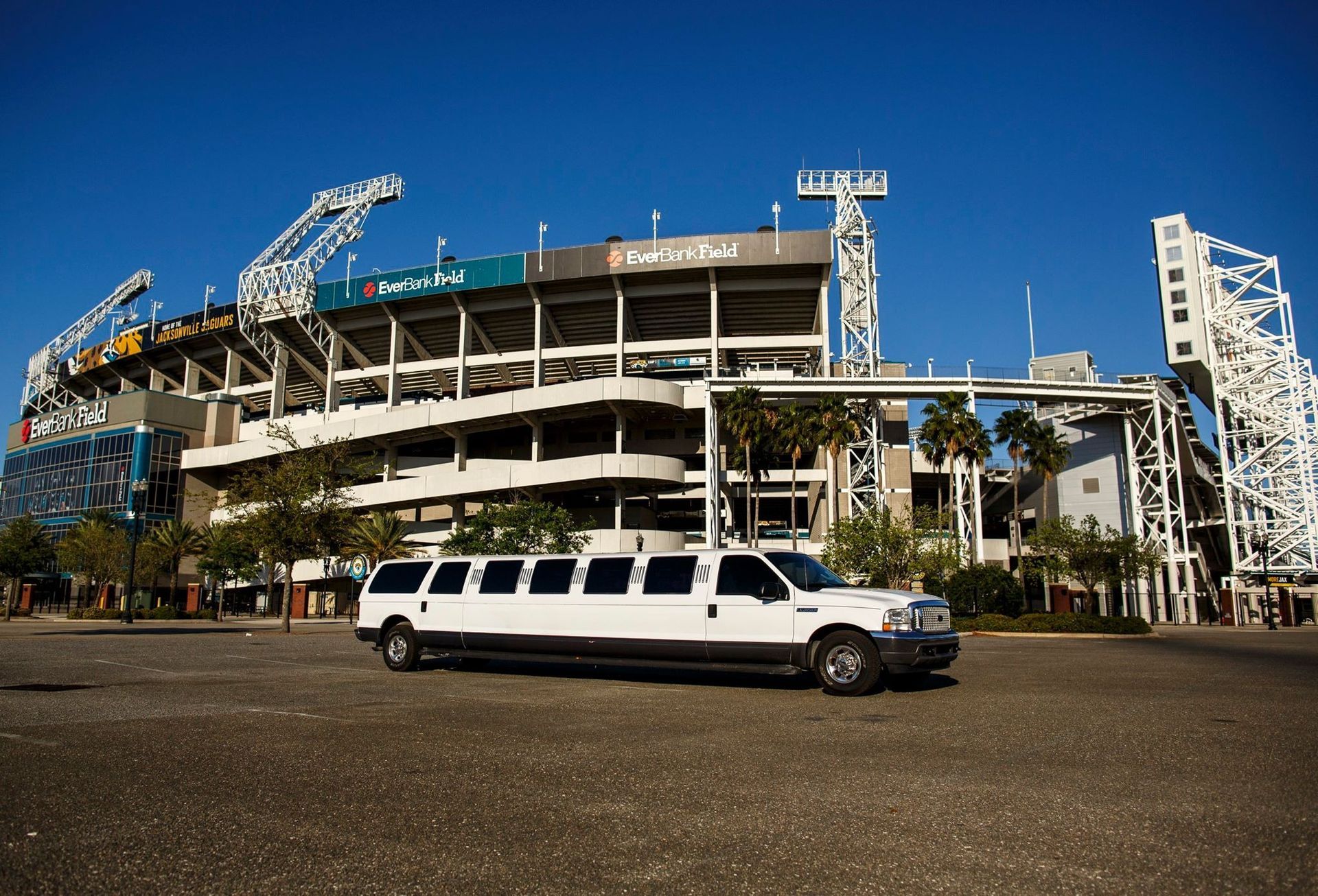 White stretch limousine parked in front of a large stadium under a clear blue sky.