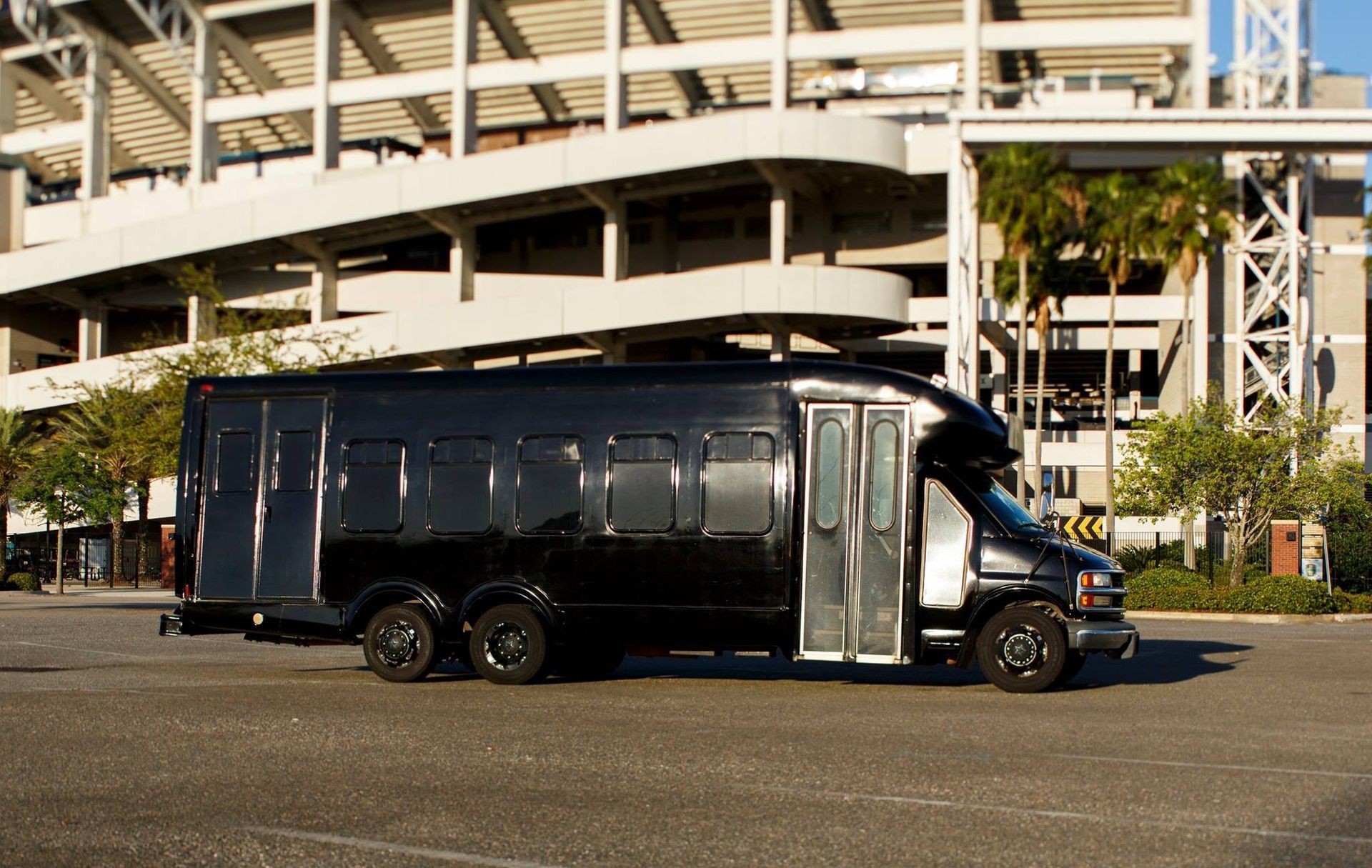Black armored bus parked outdoors in front of a building with stairs and palm trees