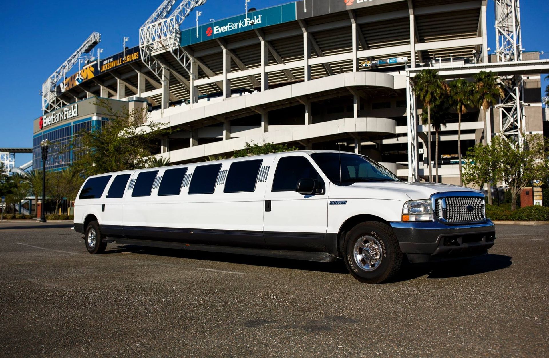 White stretched limousine parked outside a stadium on a sunny day