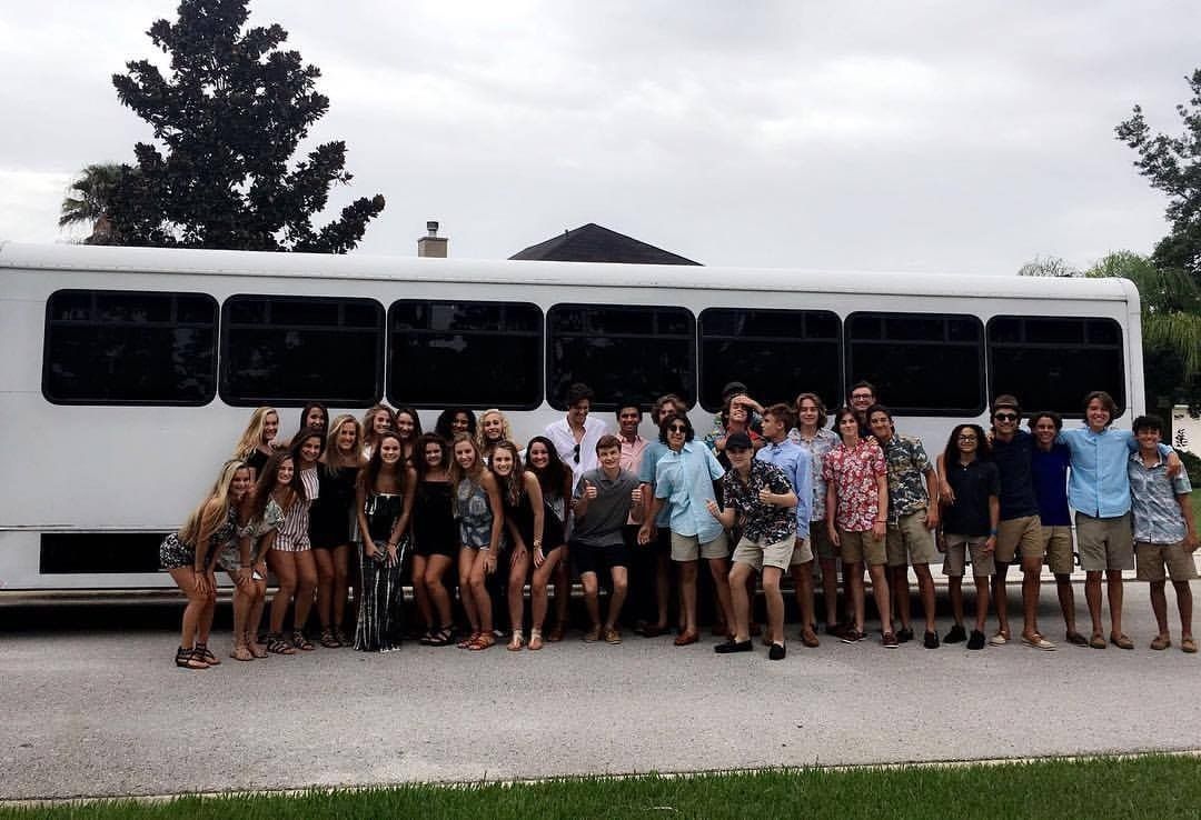 Group of people posing in front of a white bus on a road with trees behind them