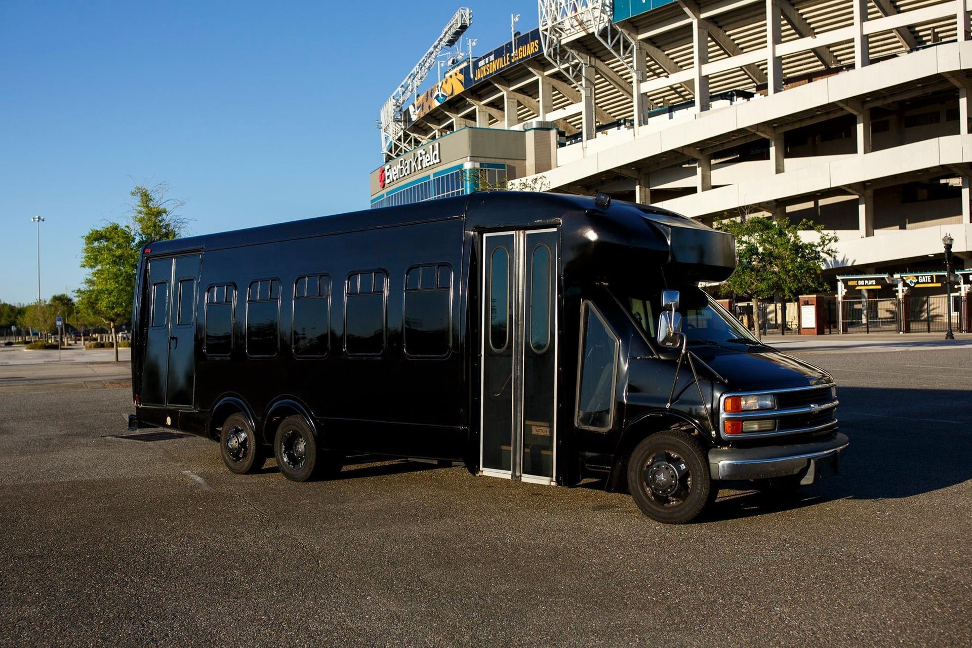 Black shuttle bus parked outside a stadium on a sunny day