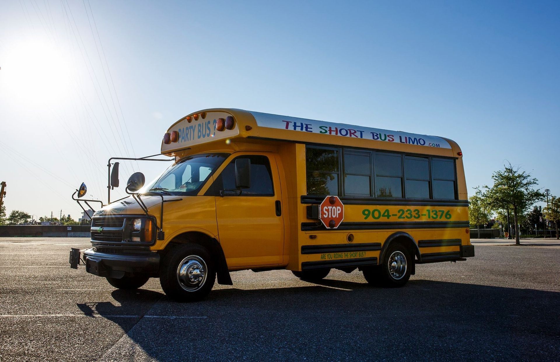 Yellow school bus parked on a road under a bright sun, side view with emergency stop sign visible