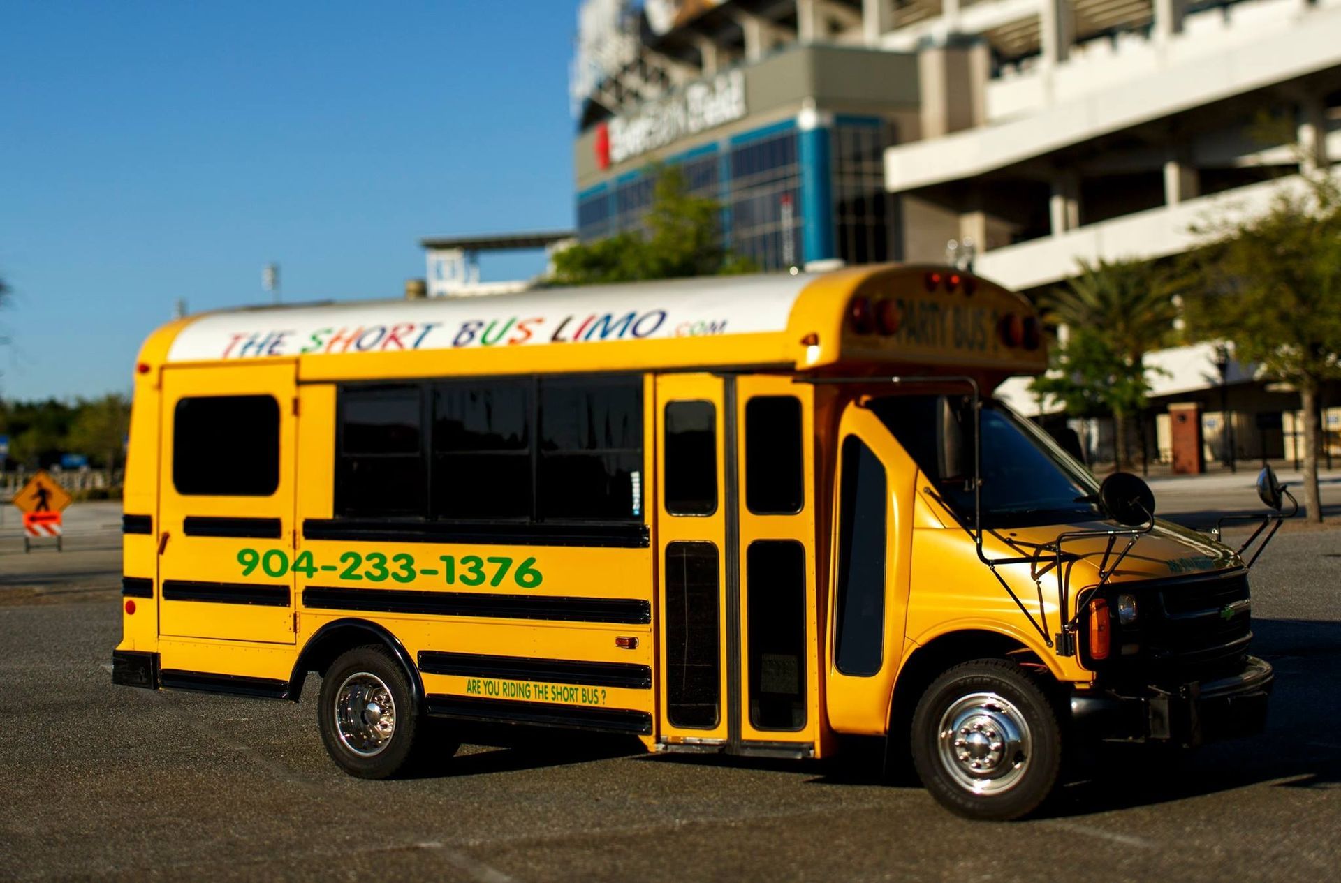 Yellow school bus parked outdoors in front of a building, with “THE BUS” on top and phone number 904-233-1376.
