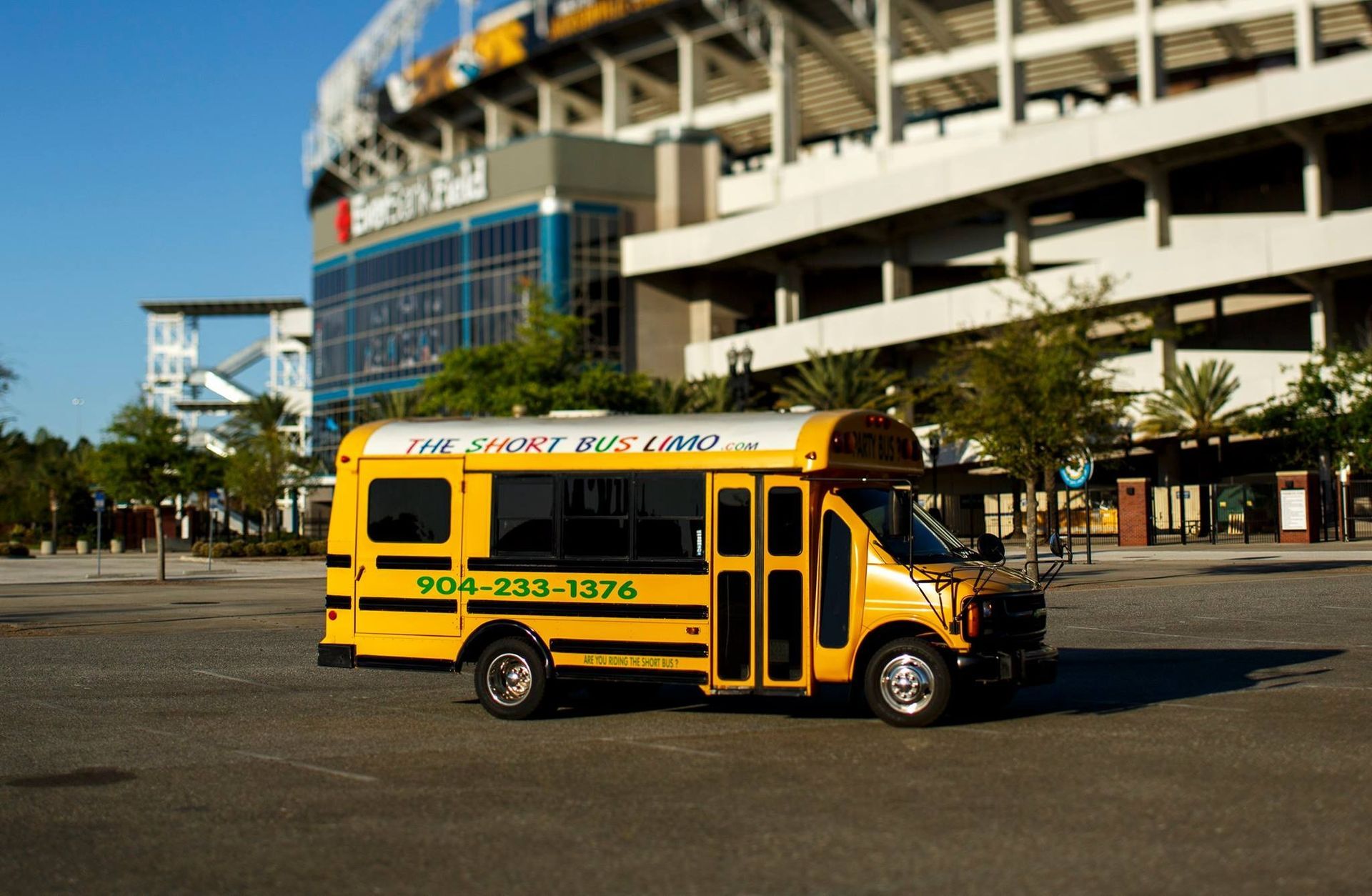 Yellow school bus parked outside a large stadium on a sunny day