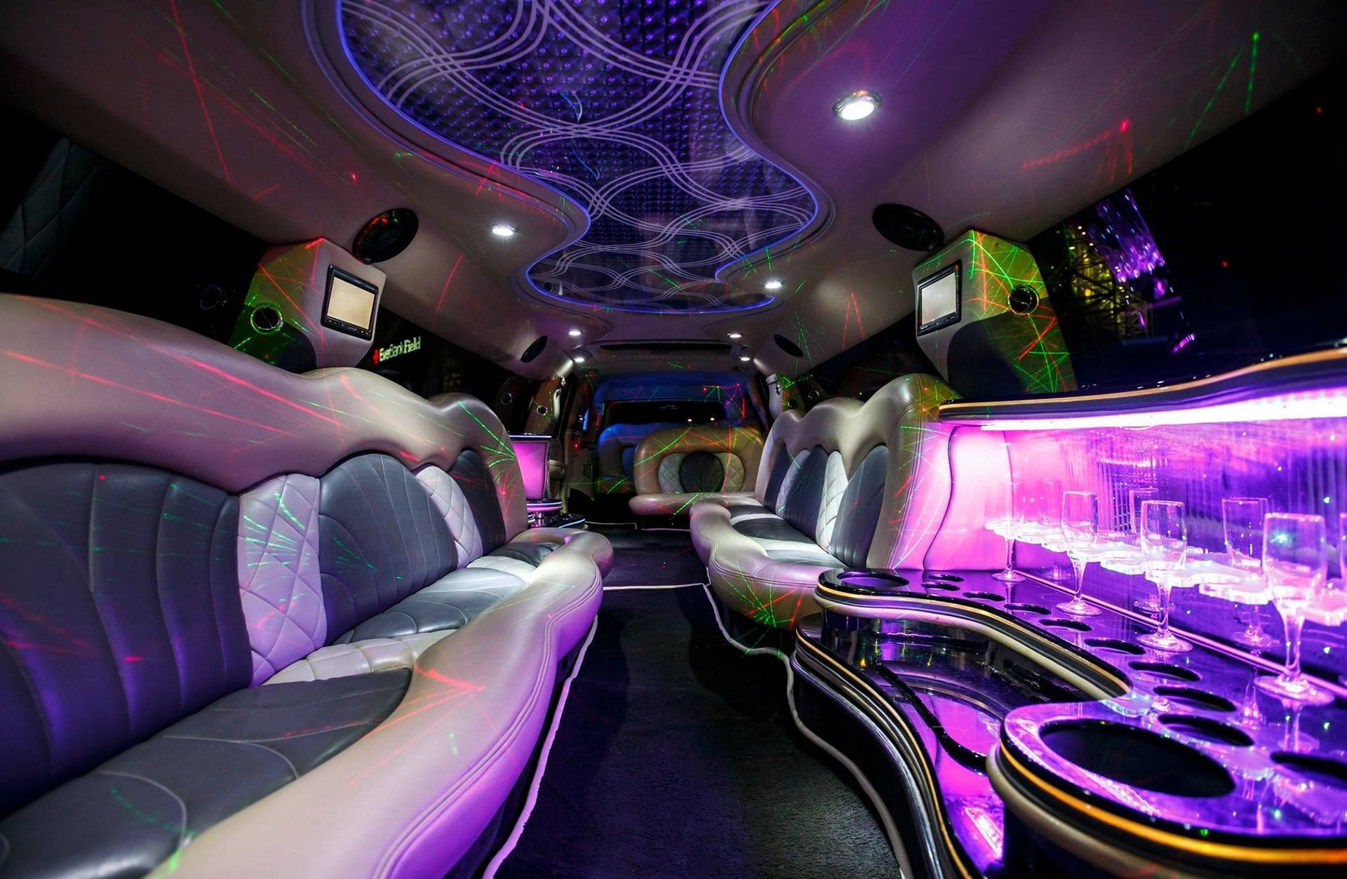 Lavish limousine interior with purple LED lighting, leather seats, and a glossy bar area