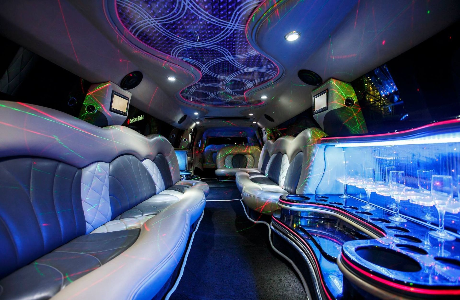 Luxury limousine interior with blue LED lighting, mirrored ceiling, and plush white leather seats