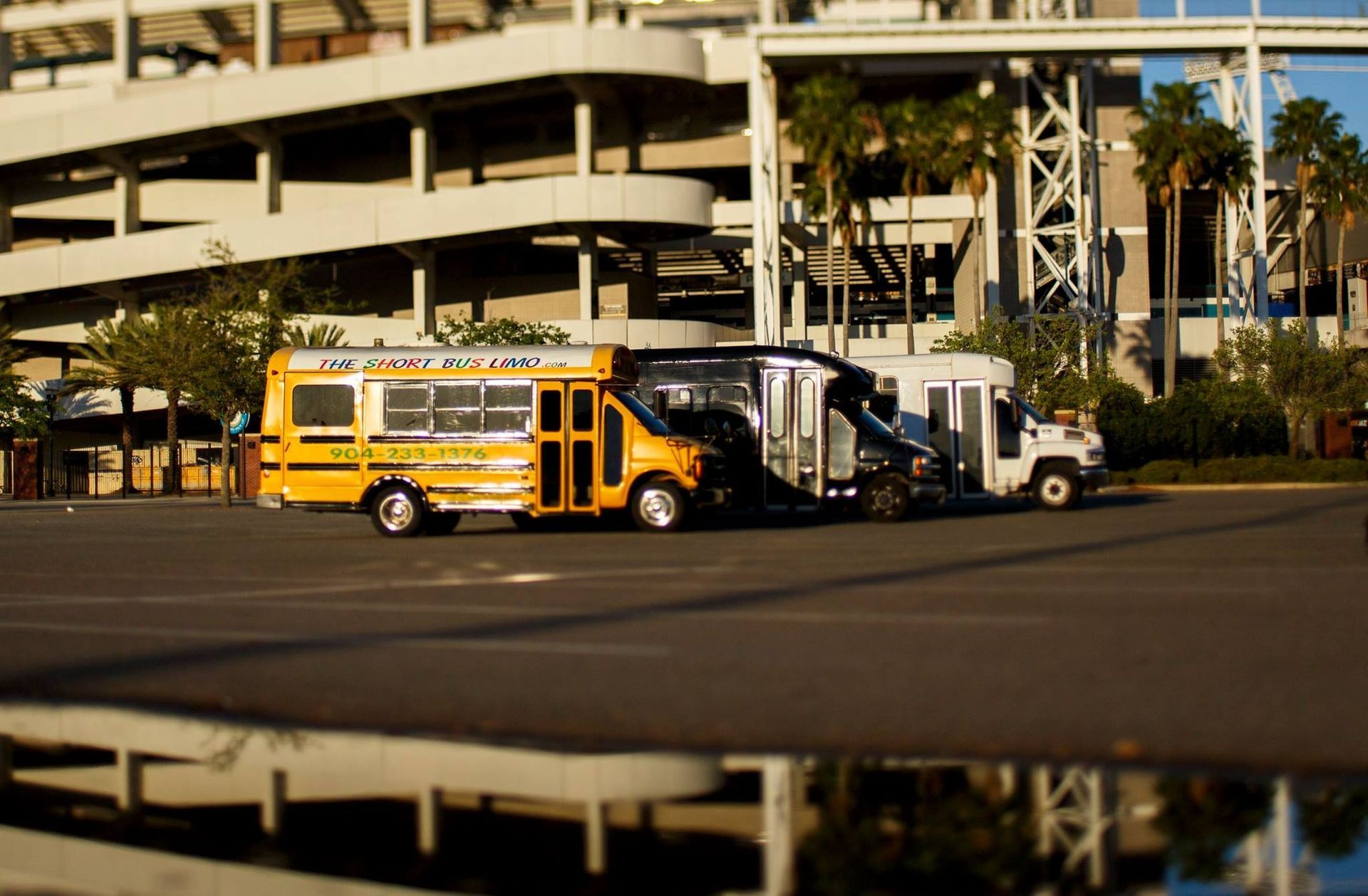 Yellow school bus and white truck parked near a multi-level parking structure, reflected in wet pavement.