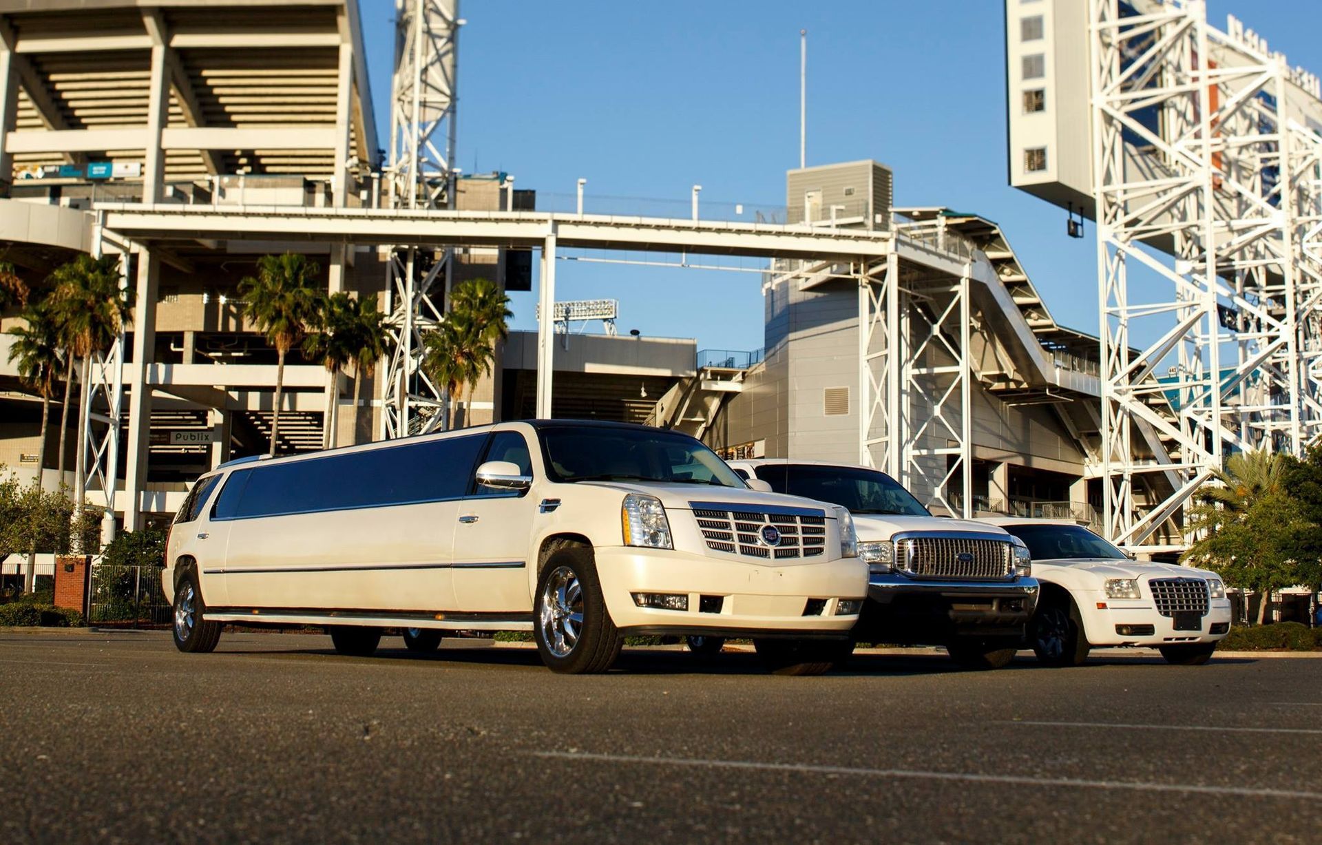 White limousine and black sedan parked on a street beside a large industrial bridge structure