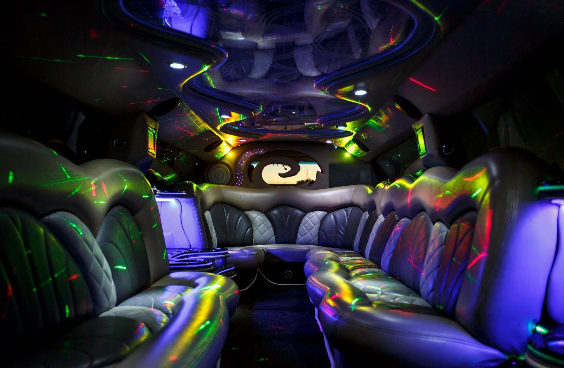 Neon-lit party bus interior with black leather seats and colorful LED lights on ceiling and walls