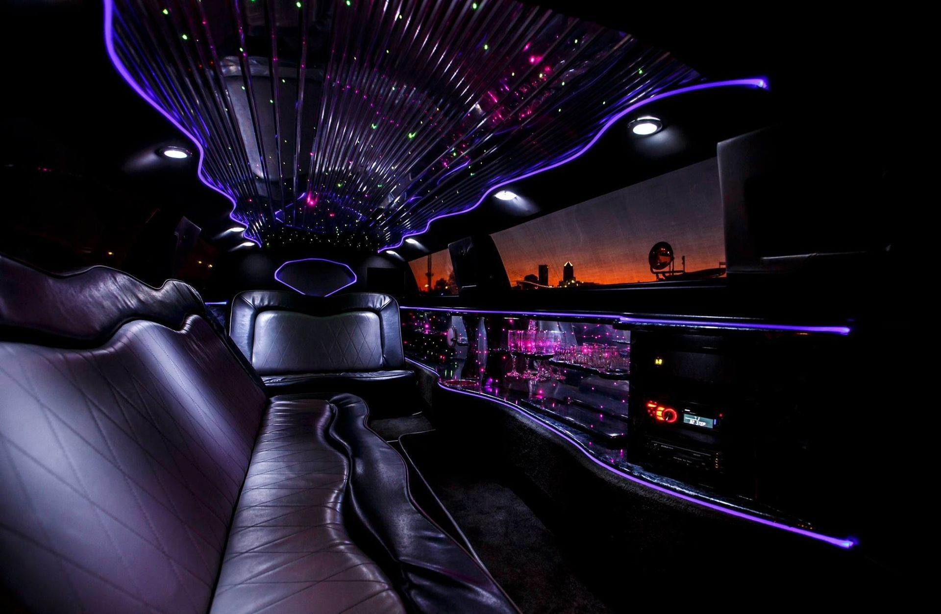 Luxury limousine interior with purple neon lighting and a sunset city view outside the window