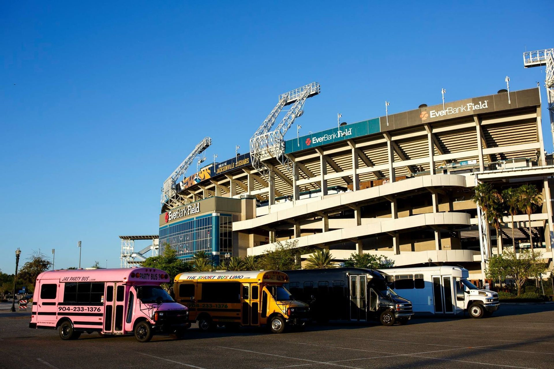 Parked buses and trucks outside a large stadium under a clear blue sky.