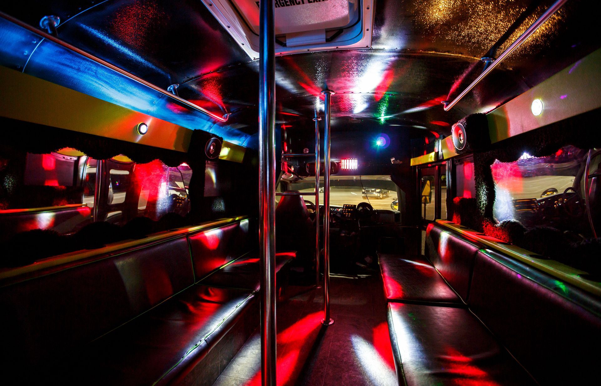 Inside a neon-lit bus interior with red, blue, and purple lights reflecting off metal poles and seats