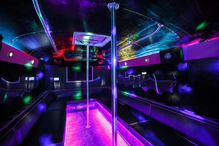 Neon-lit party bus interior with purple floor lights, chrome poles, and colorful ceiling LEDs