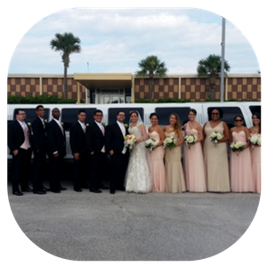 Wedding party posing in formal attire outdoors in front of a white limousine.