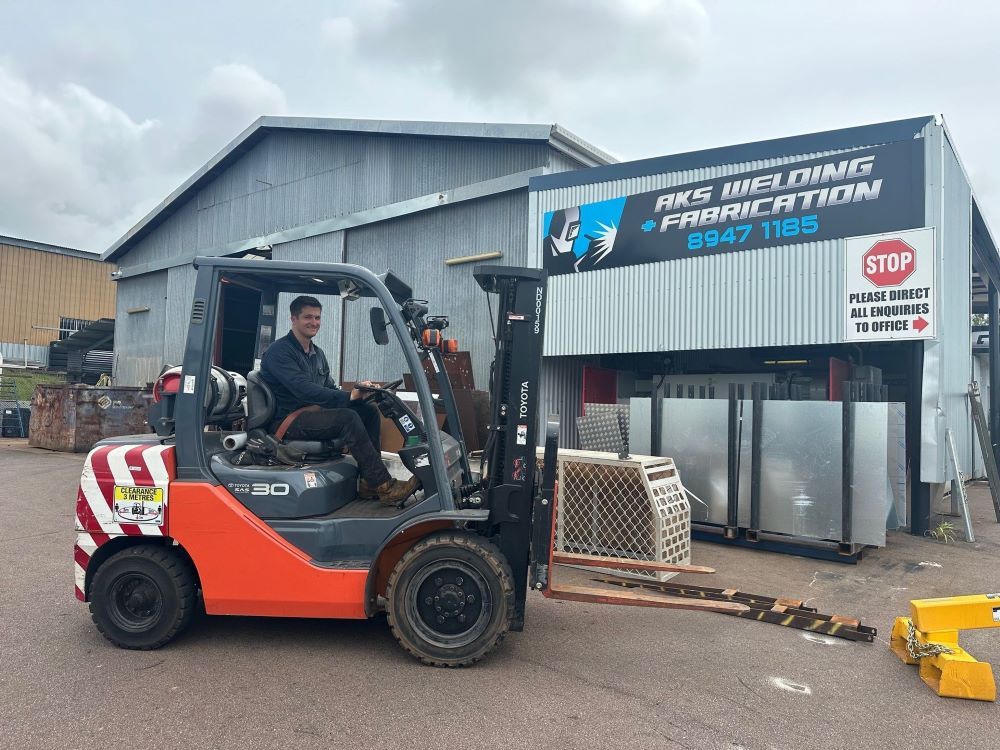 A Man is Driving a Forklift in Front of a Building — AKS Welding & Fabrication in Winnellie, NT