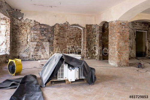 Raum im Umbau mit unverputzten Ziegelwänden, abgedeckten Geräten und einem gelben Ventilator.