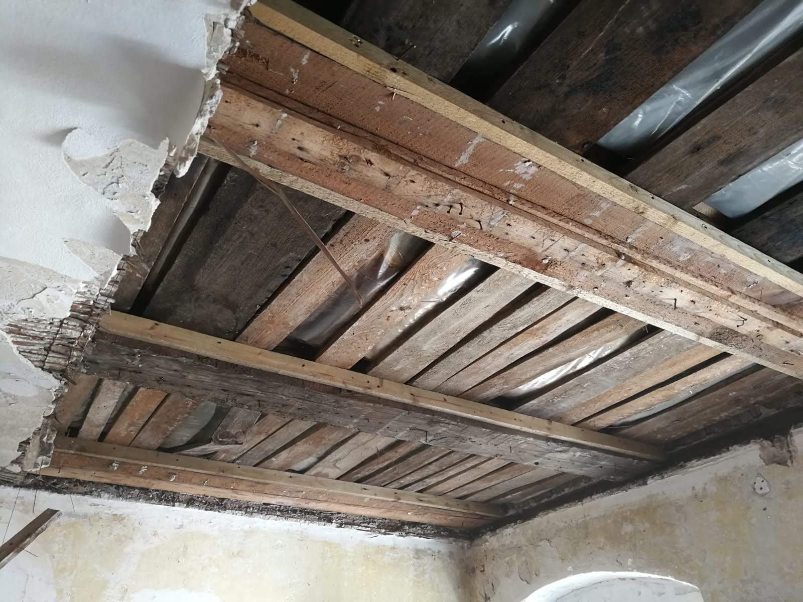 Beschädigte Decke mit freiliegenden Holzbalken und altem Putz.