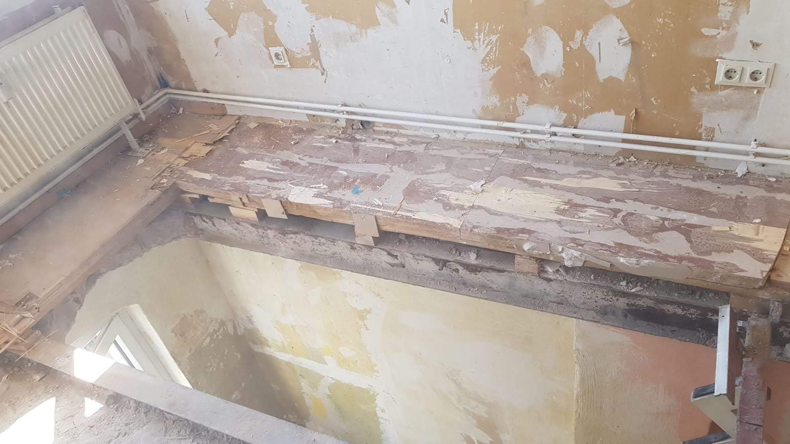 Innenansicht eines Zimmers, das gerade renoviert wird, mit beschädigtem Bodenbelag und freiliegenden Balken.