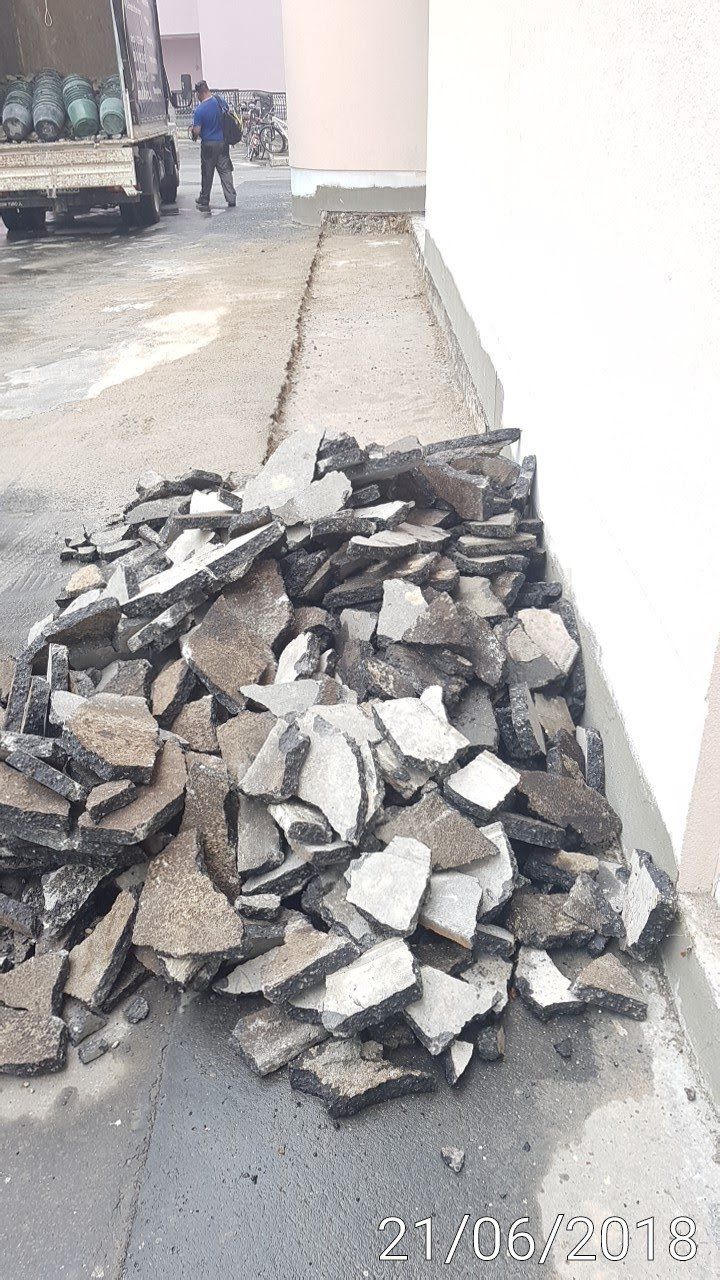 Ein Haufen gebrochenen Asphalts am Rand eines Gebäudes. Im Hintergrund sind eine Person und ein LKW zu sehen.