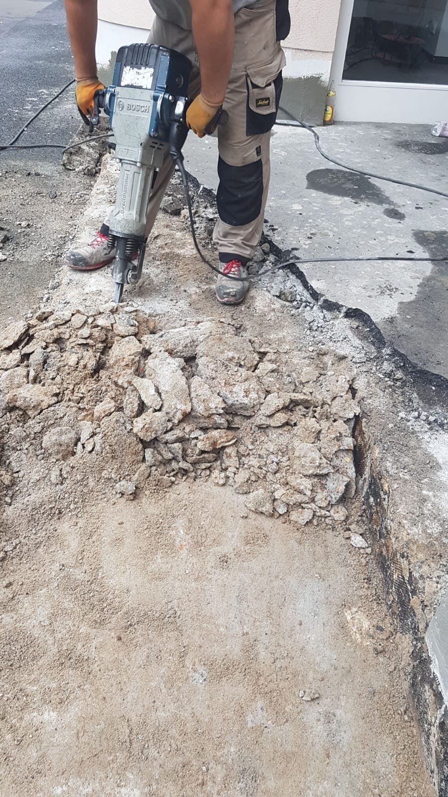 Person, die mit einem Presslufthammer Beton auf einem Gehweg aufbricht.