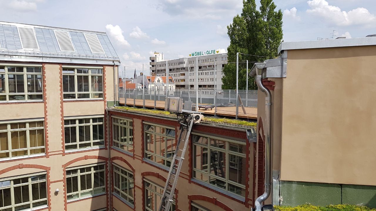 Ansicht von Gebäuden mit einem grünen Dach und einer Feuerleiter. Sonniger Tag mit blauem Himmel.