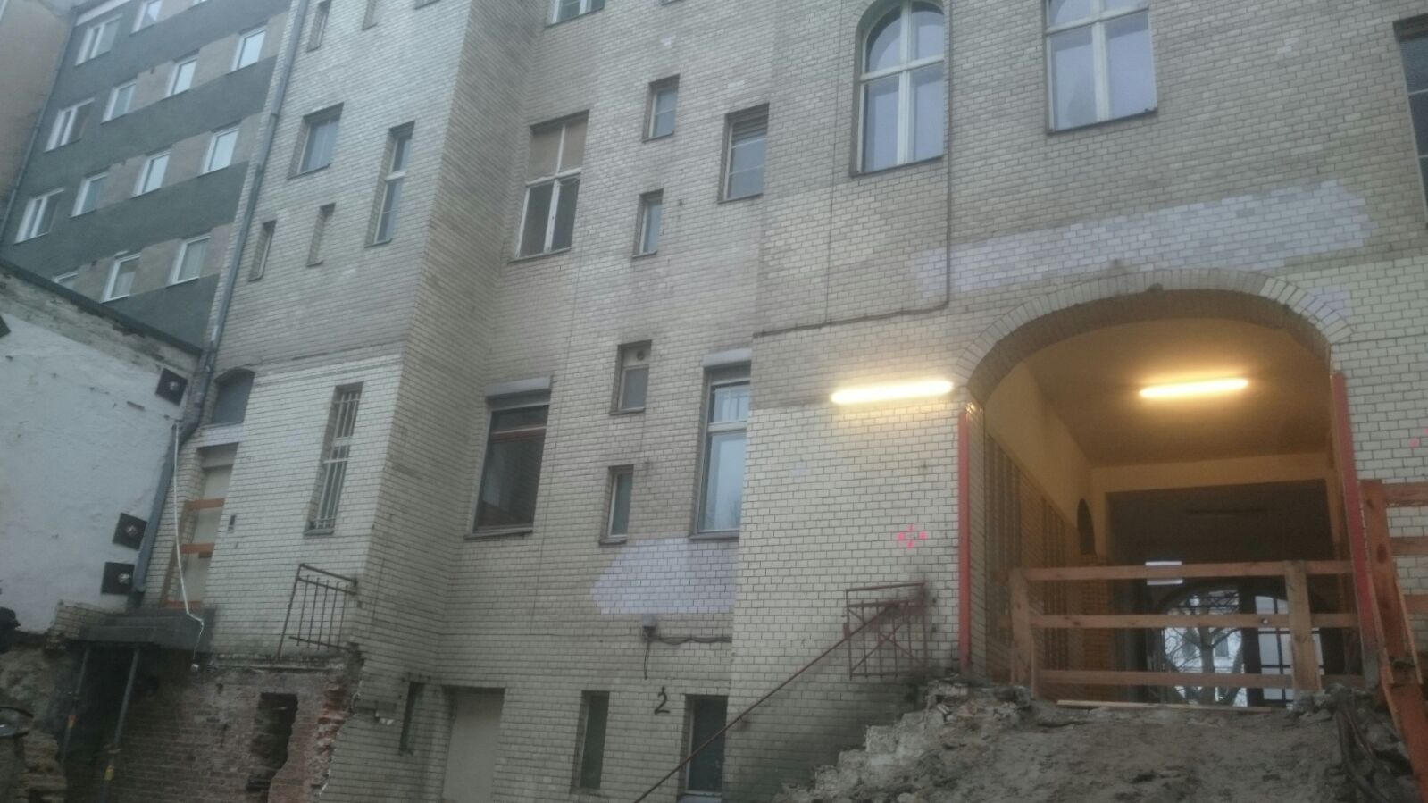 Gebäudeaußenseite mit unterschiedlich großen Fenstern und Torbogeneingang mit Konstruktion.