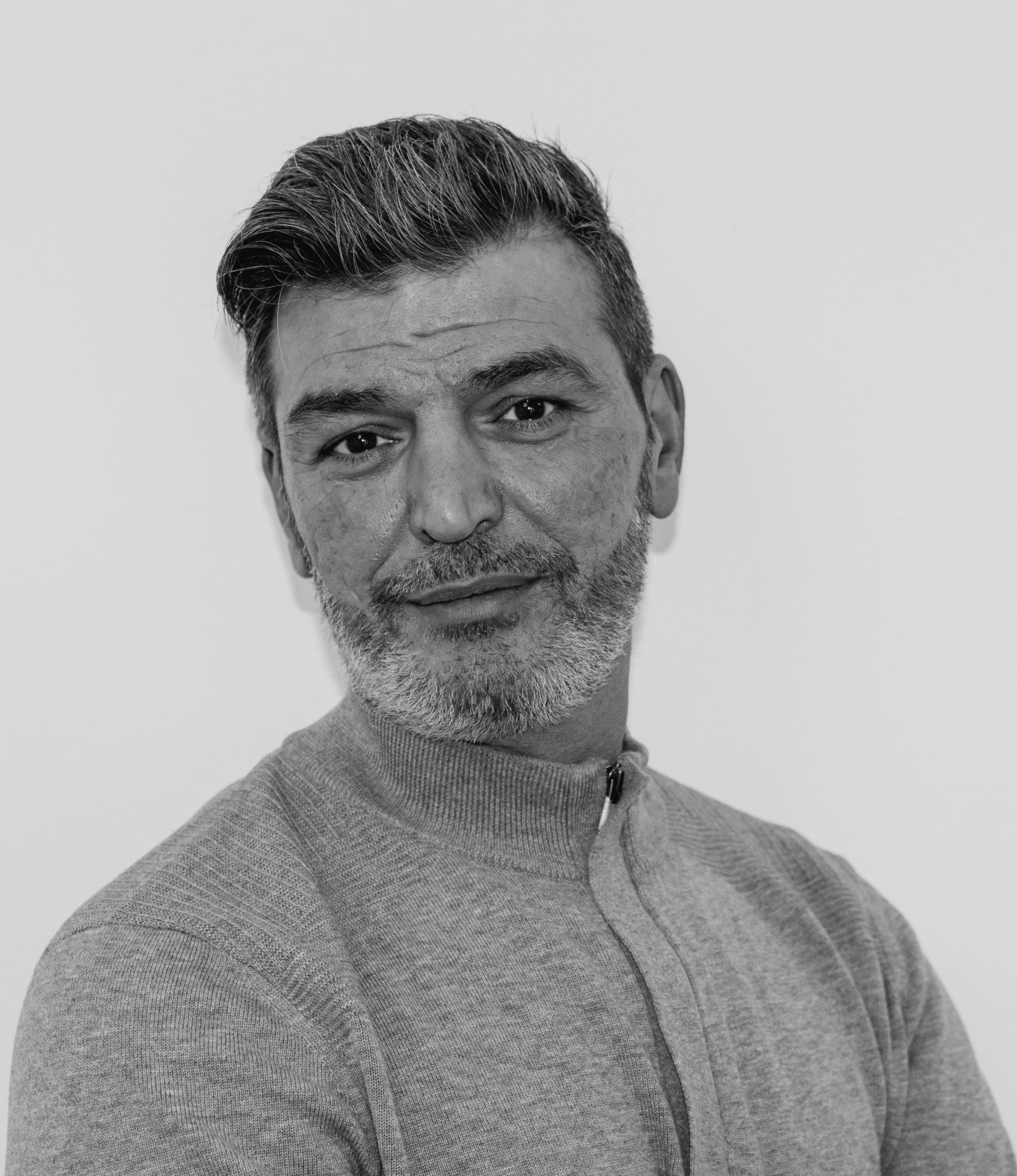 Mann mit kurzem Bart und graumeliertem Haar, grauer Pullover, blickt in die Kamera.