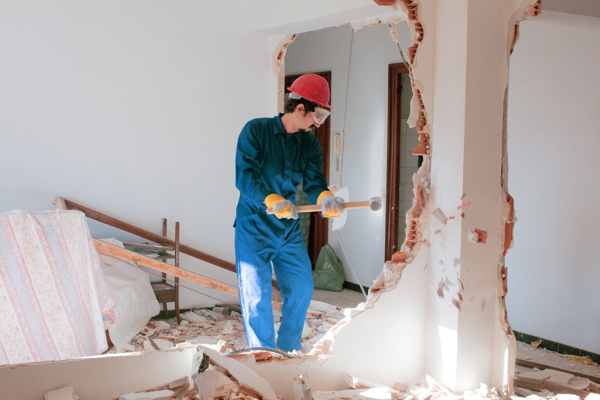 Bauarbeiter im blauen Overall reißt mit einem Vorschlaghammer eine Wand ein.