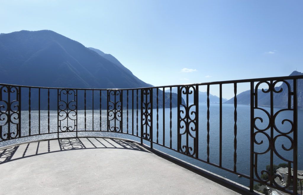 A black fence surrounds a large house with a fountain in the background.