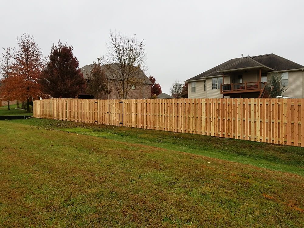 A wooden fence surrounds a grassy field in front of a house